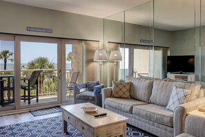 A living room with a sofa, a coffee table, and a TV. There is a balcony with a view of the ocean. - Sunset Rentals | Captains Walk 416 (Hilton Head)