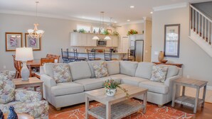 A modern living room with a sectional sofa, a coffee table, and a dining area with chairs and a table. - Sunset Rentals | Crabline 49 | Dog Friendly (Hilton Head Island)