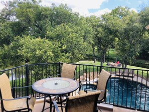 An outdoor patio with a round table and wicker chairs, overlooking a swimming pool and a grassy area with trees. - Waterfront Retreat w/ Pool, Hot Tub & Game Room (Burnet)
