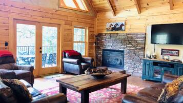 A log cabin interior with a stone fireplace, leather furniture, and a television mounted on the wall.