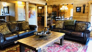 Ein rustikales Blockhaus-Interieur mit zwei Ledersofas, einem Holztisch und einem gemusterten Teppich.