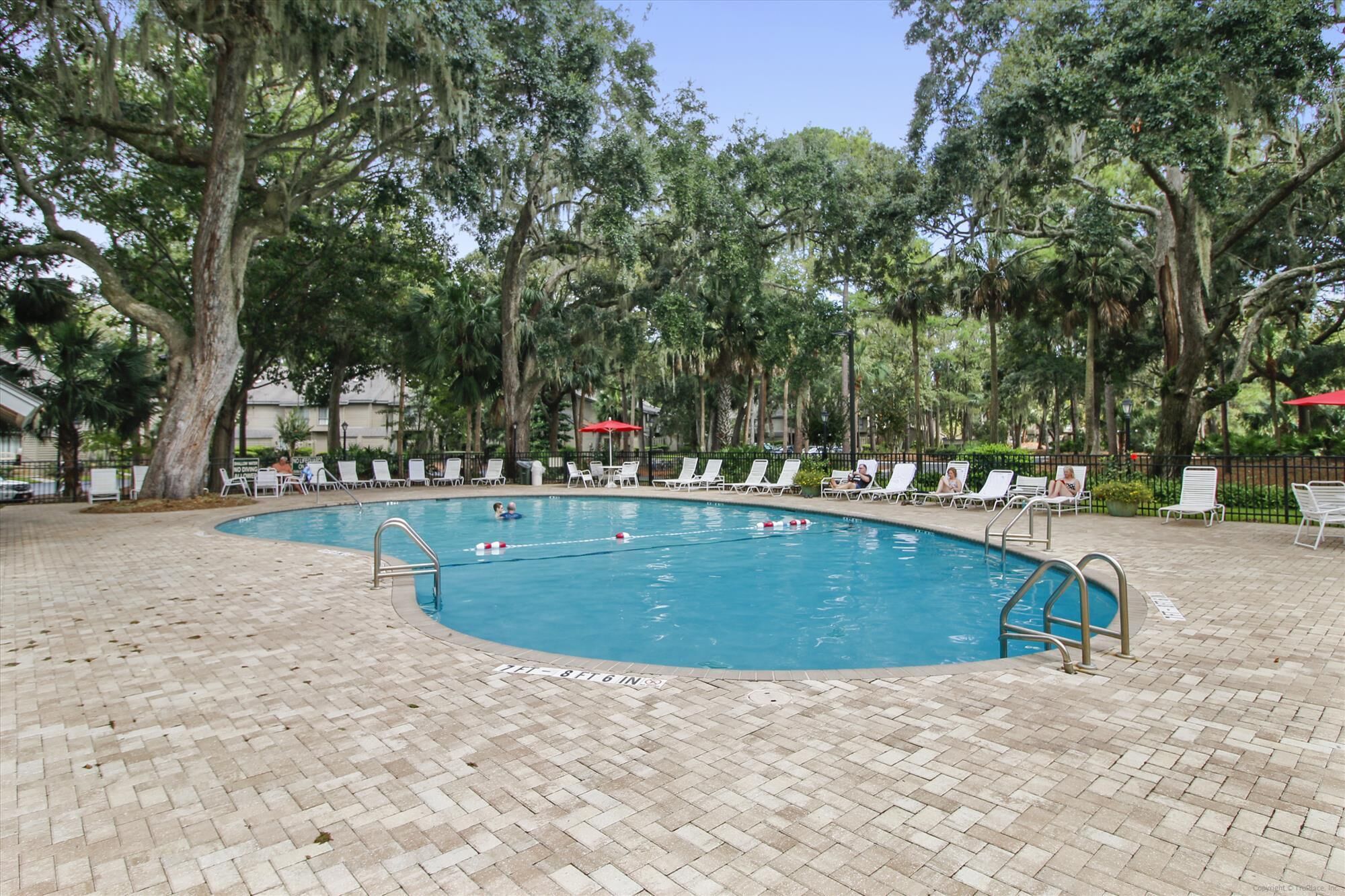 A swimming pool with a brick deck, surrounded by trees and lounge chairs.