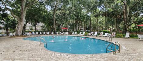 A swimming pool with a brick deck, surrounded by trees and lounge chairs.