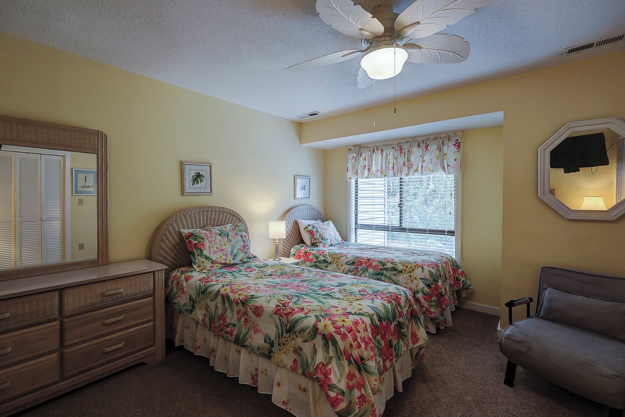 A bedroom with two beds, a dresser, a chair, a ceiling fan, and a window with blinds.