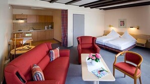 Habitación de hotel compacta con sofá rojo, una pequeña mesa de comedor, una cama individual y una kitchenette.