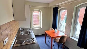 Eine kleine Küche mit Kochfeld, Spüle und Fenster. Ein kleiner Esstisch mit Stühlen steht bereit.