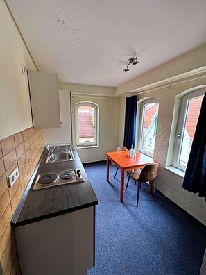 A compact kitchen with a stove, sink, and window. There is a small dining table with chairs.
