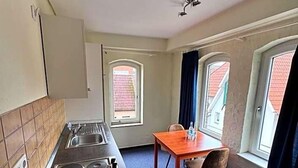 Una cocina compacta con estufa, lavamanos y ventana. Hay una pequeña mesa de comedor con sillas.