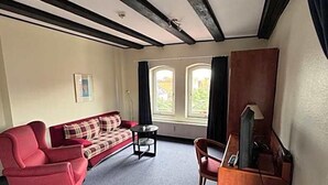 Quarto com sofá vermelho, uma mesinha, um suporte para TV e janela com cortinas.