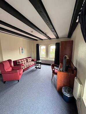 A room with a red sofa, a small table, a TV stand, and a window with curtains.
