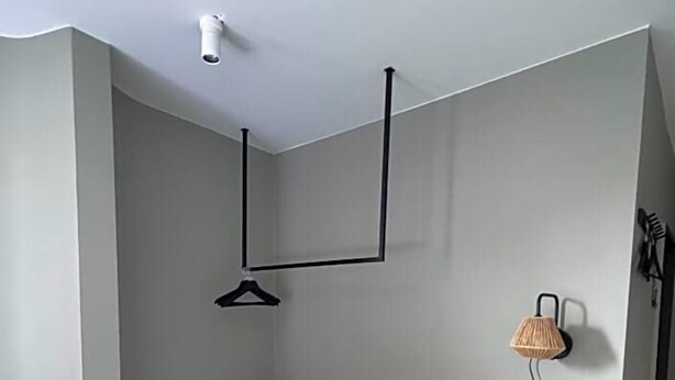 Una habitación pequeña y moderna con un escritorio de madera, una sola silla, una lámpara colgante y un cubo de basura negro.