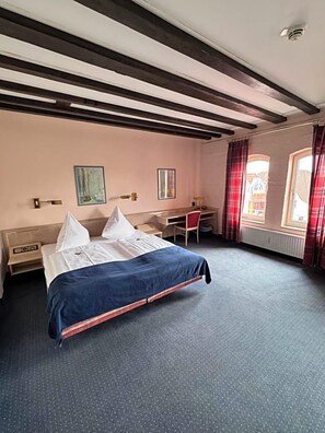 A hotel room with a bed, desk, chair, and a window with curtains.