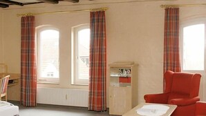 Una habitación con un sillón rojo, una mesita y un aparador con vajilla.
