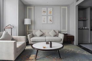 A modern living room with a sofa, armchair, and coffee table. There is a lamp, a small table with a vase, and framed artwork on the wall. - Hopesun Hotel (Jiangyin)
