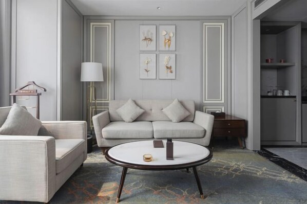 A modern living room with a sofa, armchair, and coffee table. There is a lamp, a small table with a vase, and framed artwork on the wall. - Hopesun Hotel (Jiangyin)