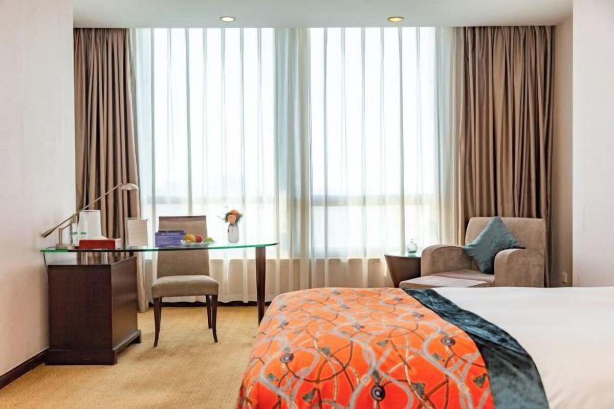 Habitación de hotel con cama, escritorio, silla y ventana con cortinas.