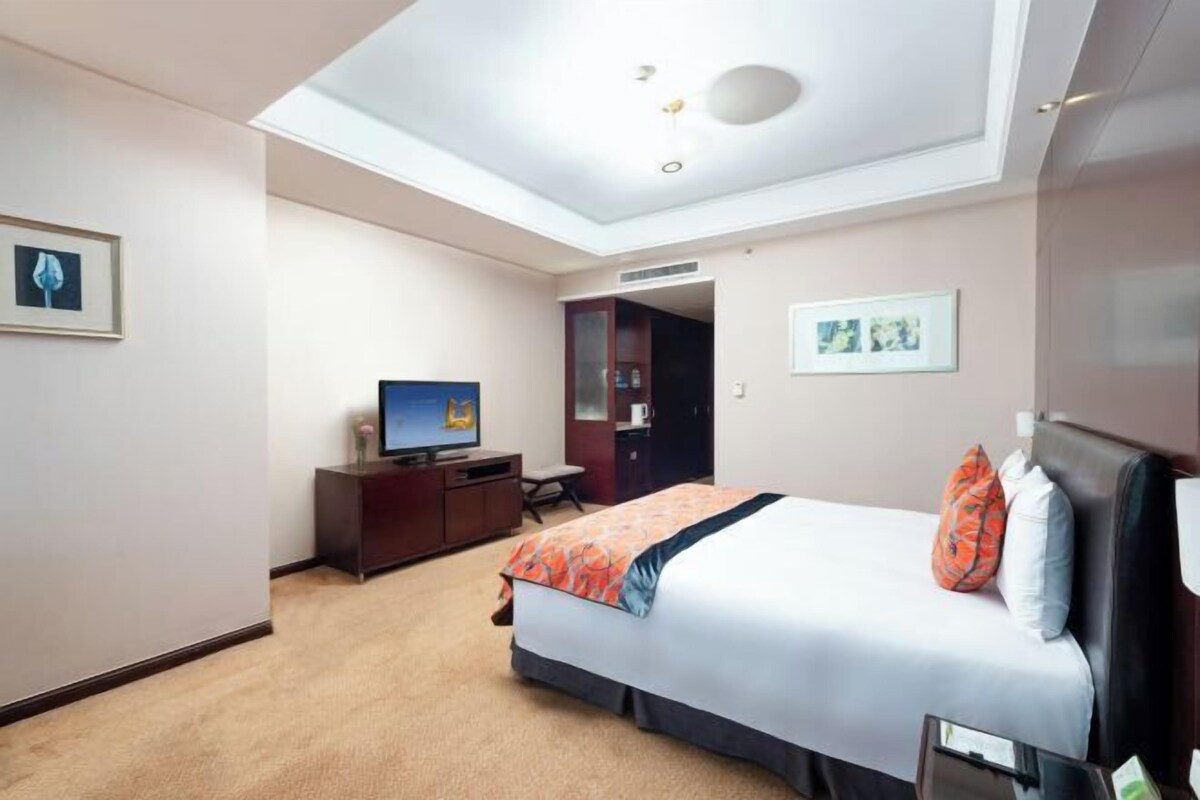 A hotel room with a bed, a desk, a television, and a ceiling light.