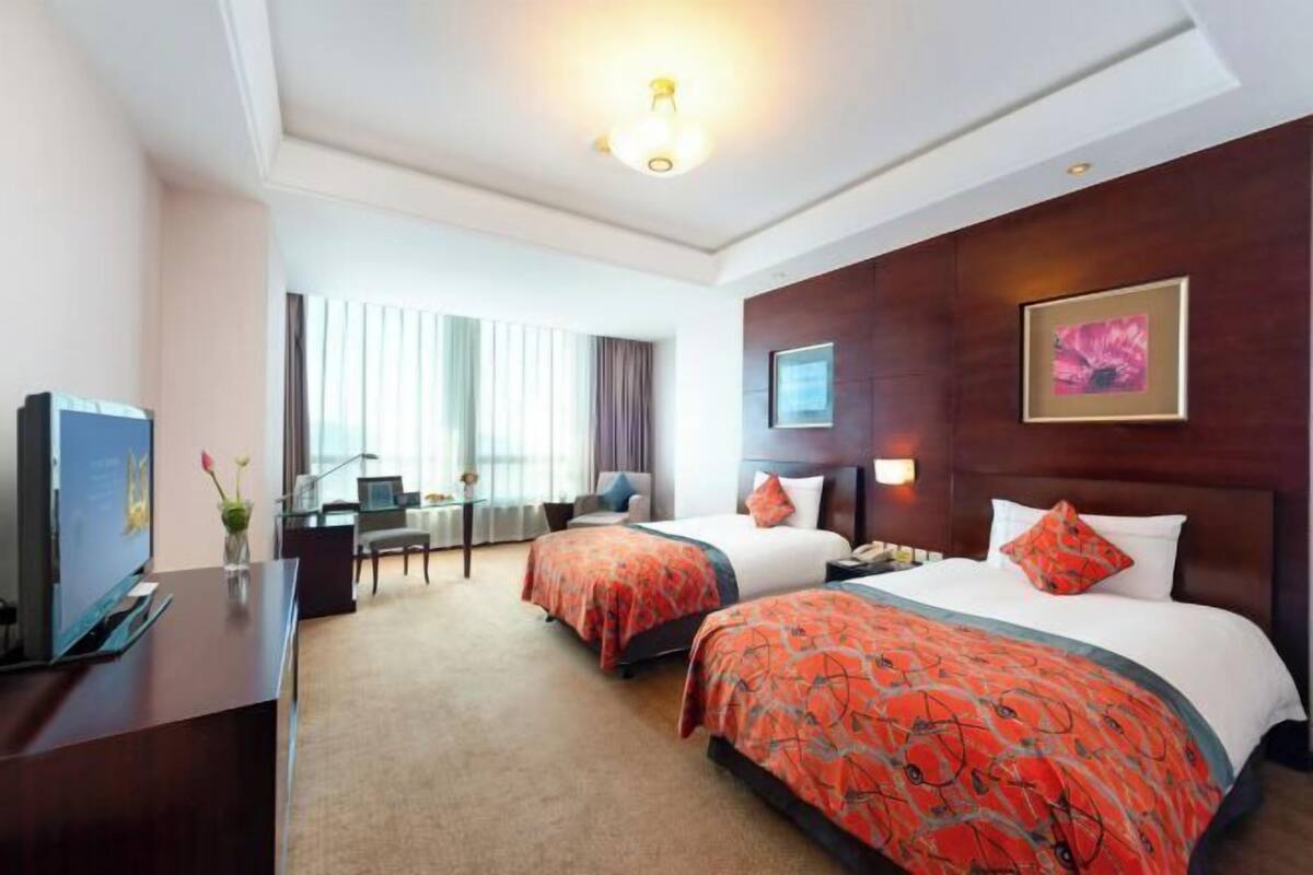 A hotel room with two beds, a desk, a TV, and a window with curtains.