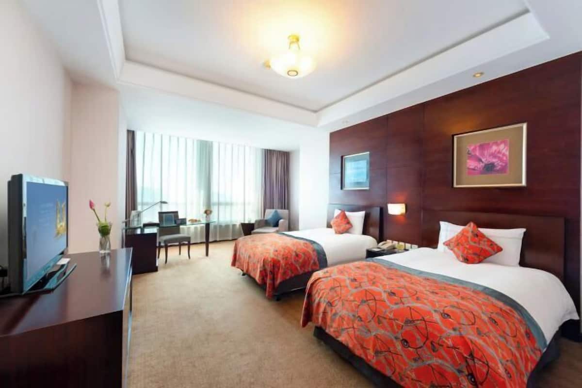 A hotel room with two beds, a desk, a TV, and a window with curtains.