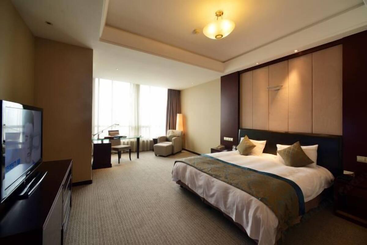 A hotel room with a large bed, a TV, a desk with a chair, and a window.