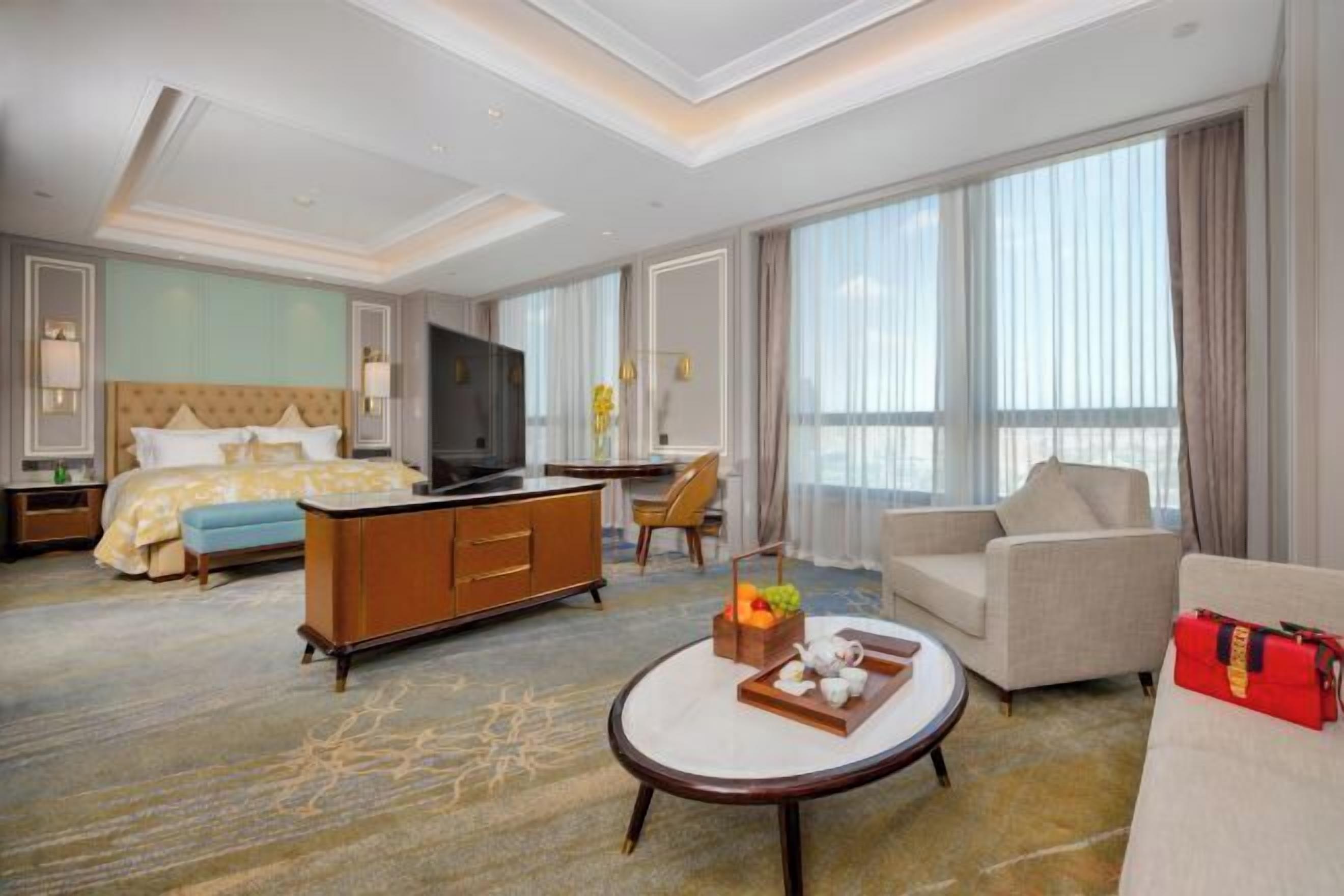 A hotel room with a bed, a sofa, a coffee table, a TV, and a large window.