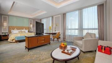 A hotel room with a bed, a sofa, a coffee table, a TV, and a large window.