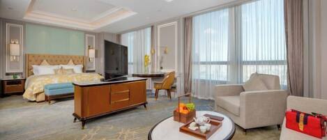 A hotel room with a bed, a sofa, a coffee table, a TV, and a large window.