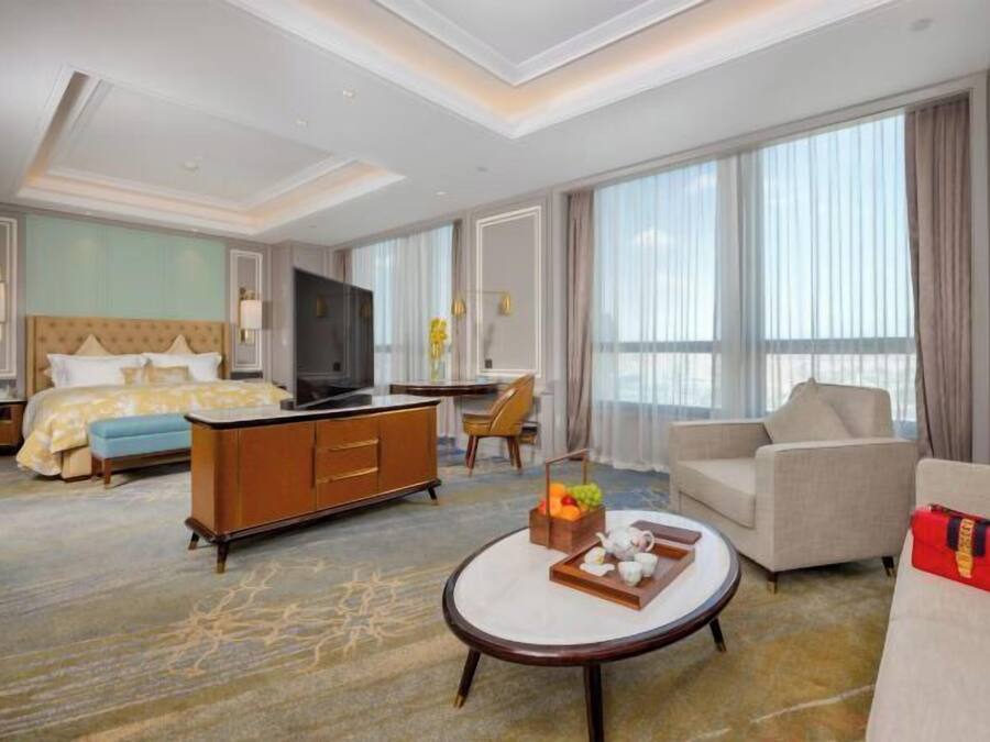 A hotel room with a bed, a sofa, a coffee table, a TV, and a large window.