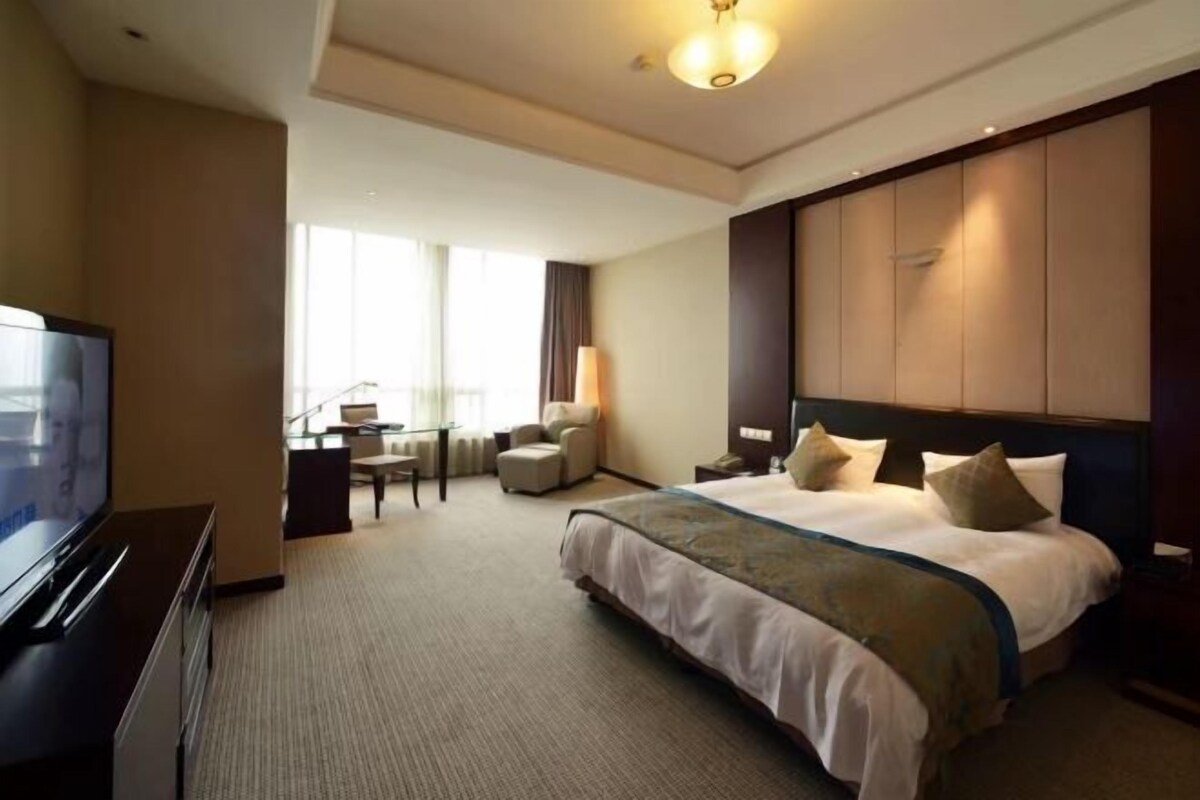 A hotel room with a large bed, a TV, a desk, and a chair.
