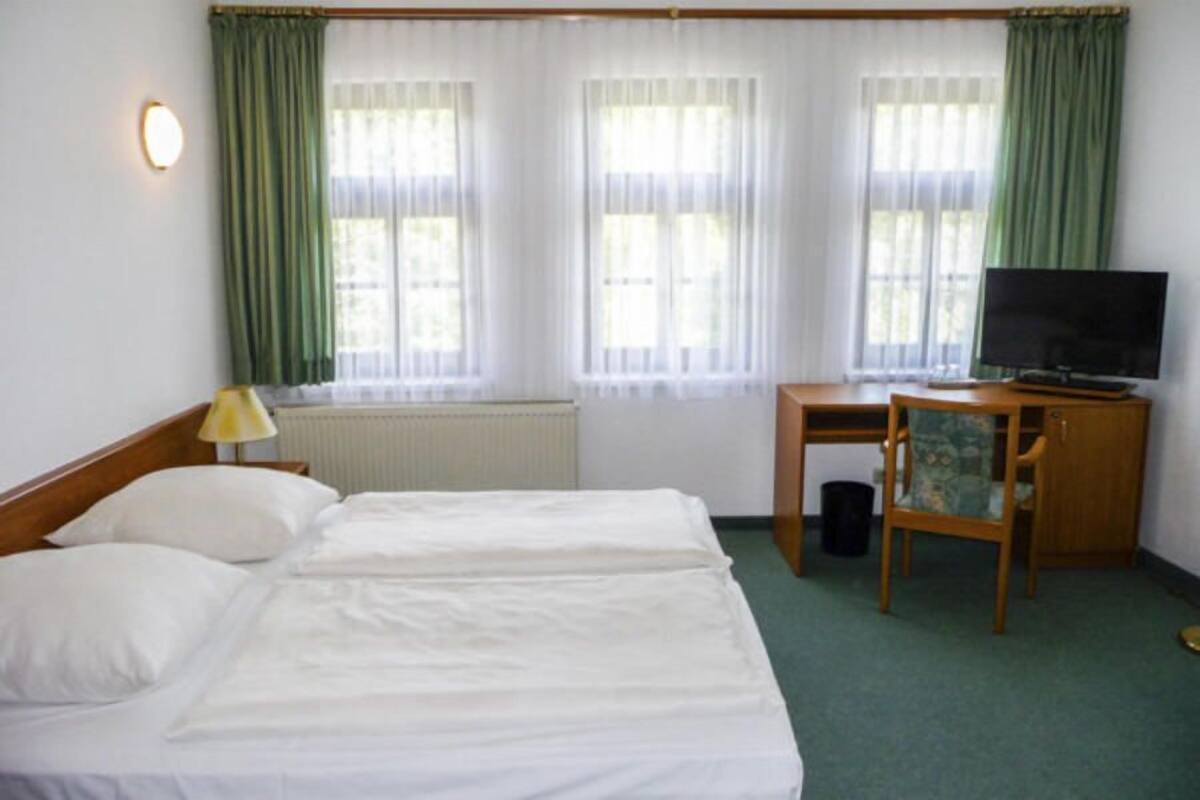 A hotel room with two beds, a desk with a television, and a radiator.