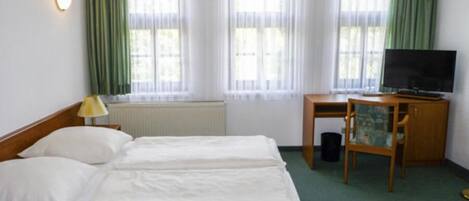 A hotel room with two beds, a desk with a television, and a radiator.