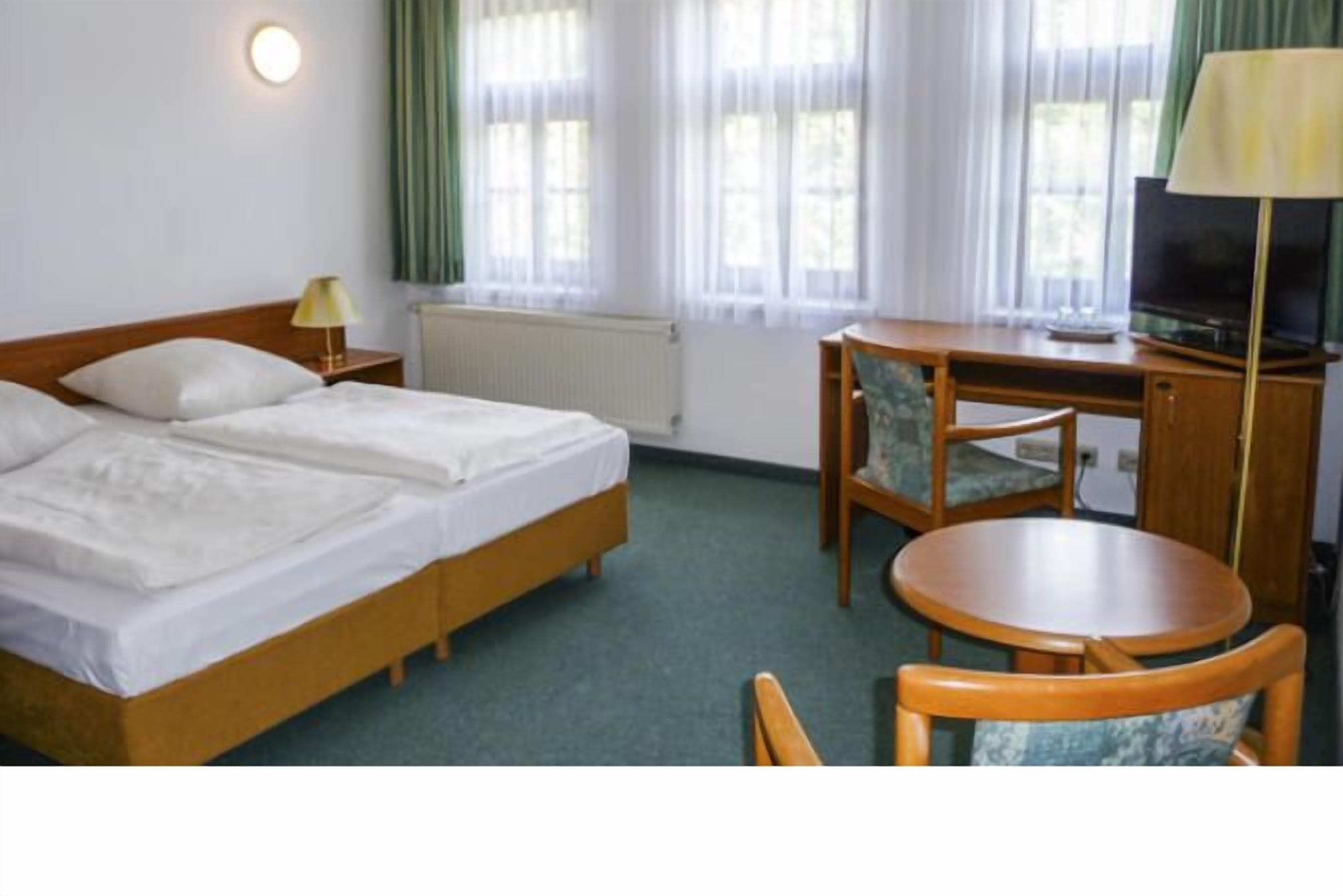 A hotel room with a double bed, a desk with a chair, a television, and a lamp.