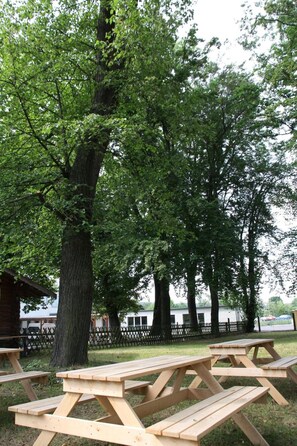 A picnic area with wooden tables and benches, surrounded by trees and a fence. - Landhaus Falkenstein (Tambach-Dietharz)