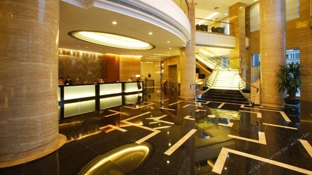 Een moderne hotel lobby met een receptiebalie, een trap en een gepolijste marmeren vloer.