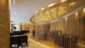 Een moderne hotellobby met een gebogen zithoek, een glazen scheidingswand en een hoge plafond met inbouwverlichting.