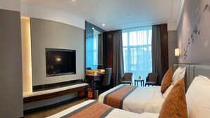 Een hotelkamer met twee bedden, een televisie, een bureau met stoel en een raam met gordijnen.