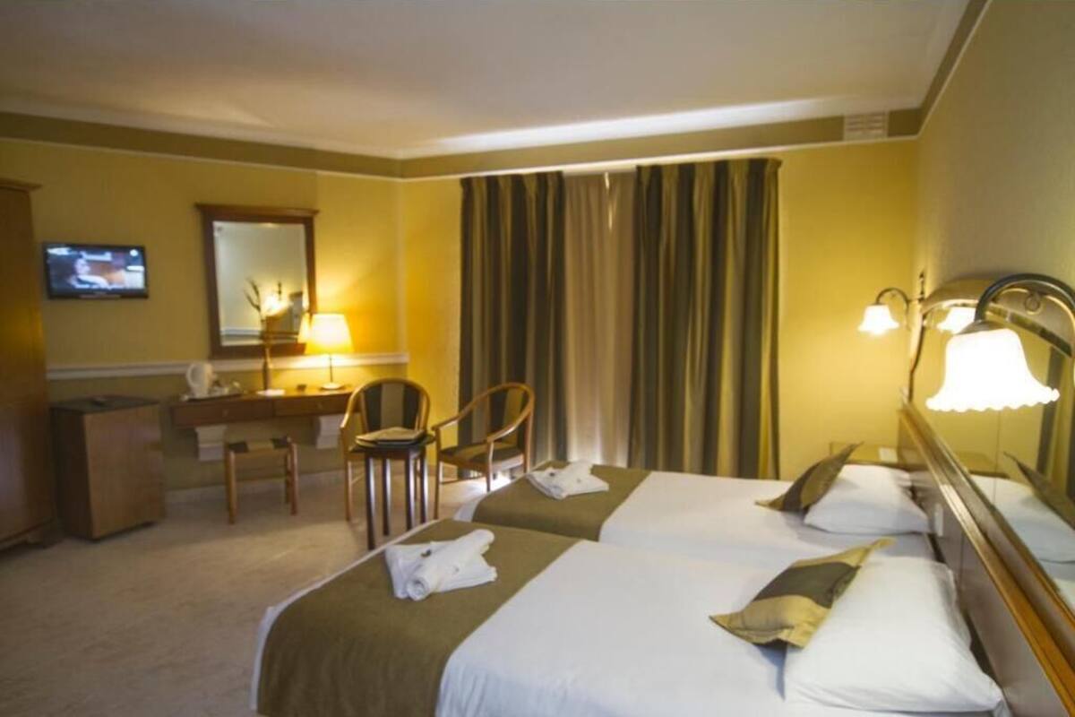 A hotel room with two beds, a desk, a chair, a television, and a large window with curtains.