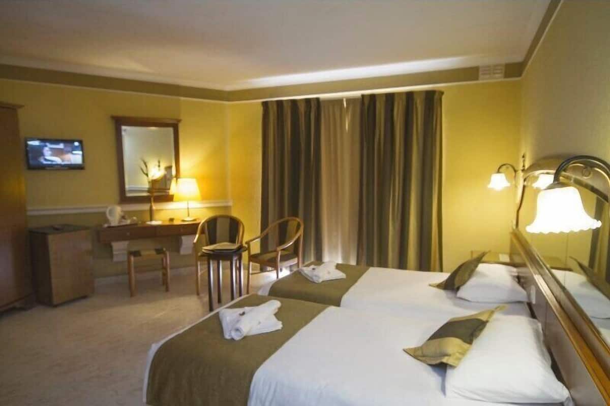 A hotel room with two beds, a desk, a chair, a TV, and a large window with curtains.