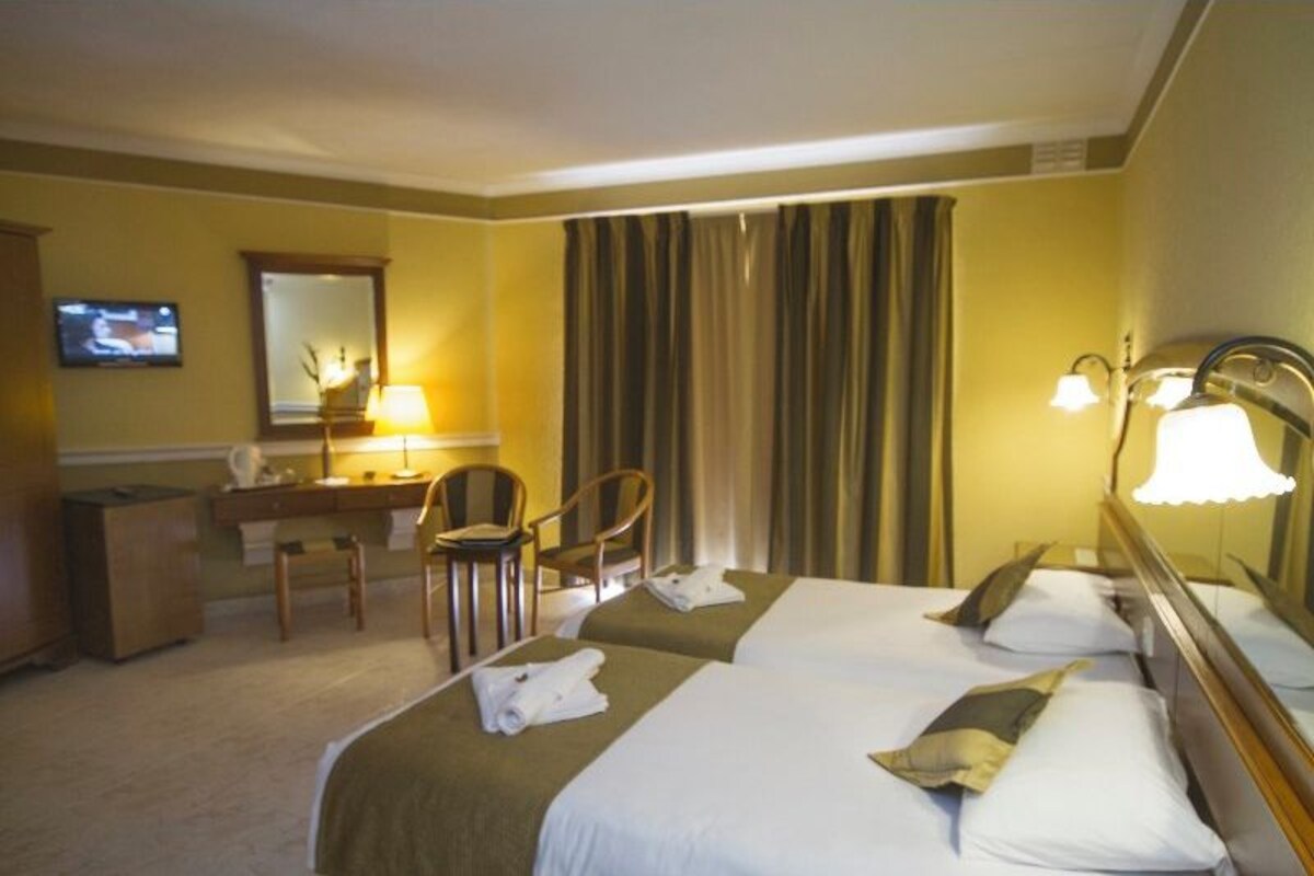 Habitación de hotel con dos camas, un escritorio, una silla, televisión y un amplio ventanal con cortinas.