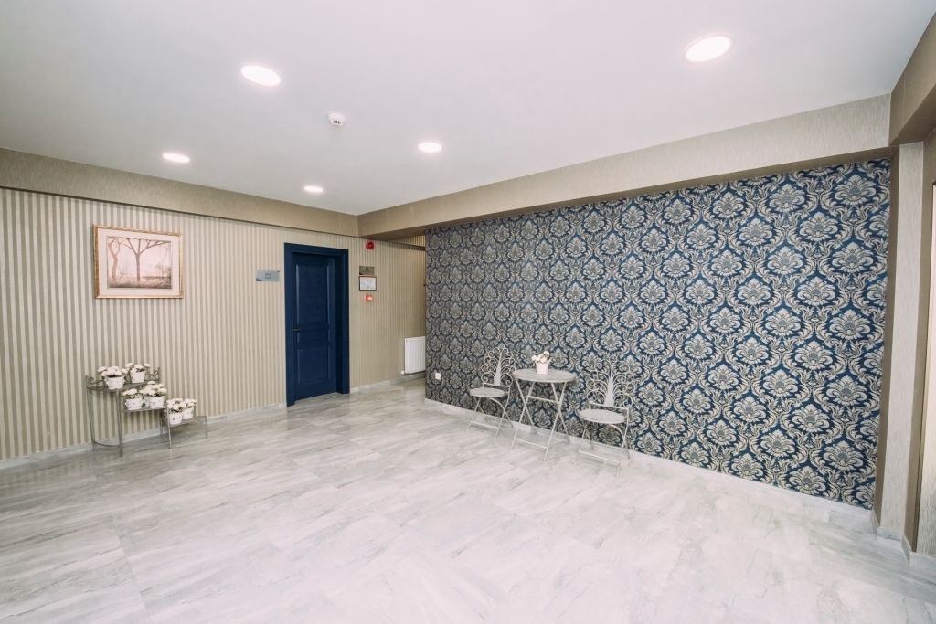 Un'ampia stanza con una parete decorata, una porta e un'area salotto con tavoli e sedie.
