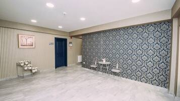 Un'ampia stanza con una parete decorata, una porta e un'area salotto con tavoli e sedie.