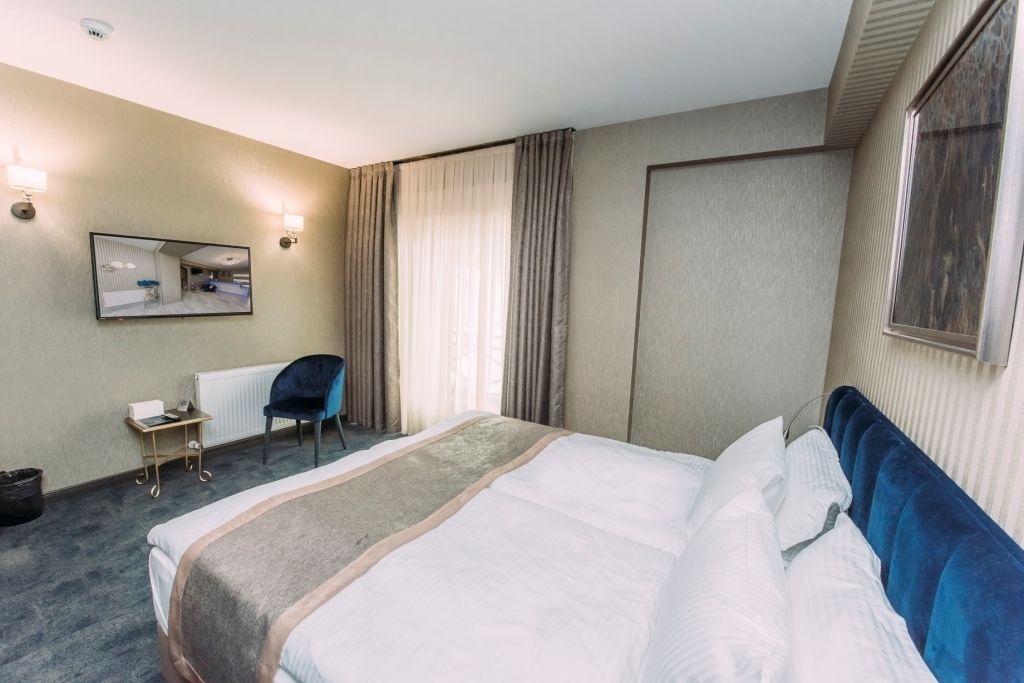 A hotel room with a large bed, a chair, a desk, and a mirror.