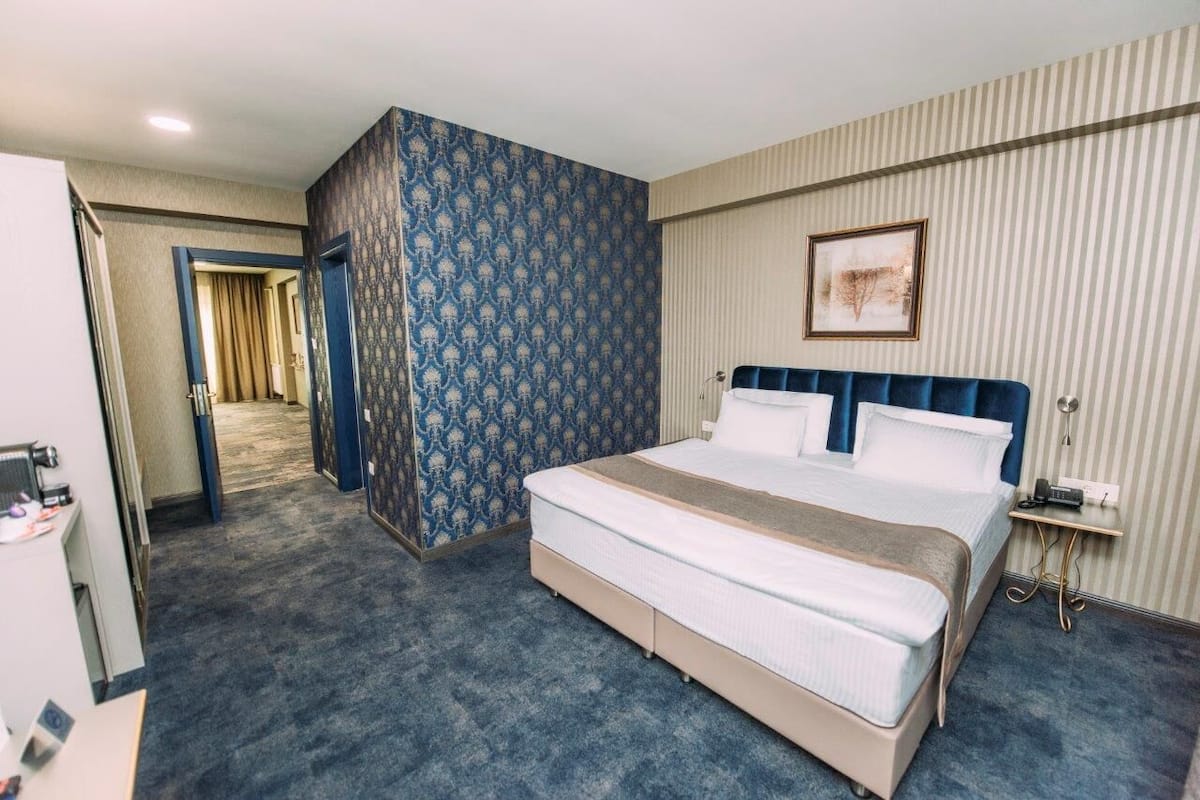 Ein Hotelzimmer mit einem großen Bett, einem Schreibtisch mit Stuhl, einem Kleiderschrank und einem durchgegangene Tür erkennbaren Badezimmer.