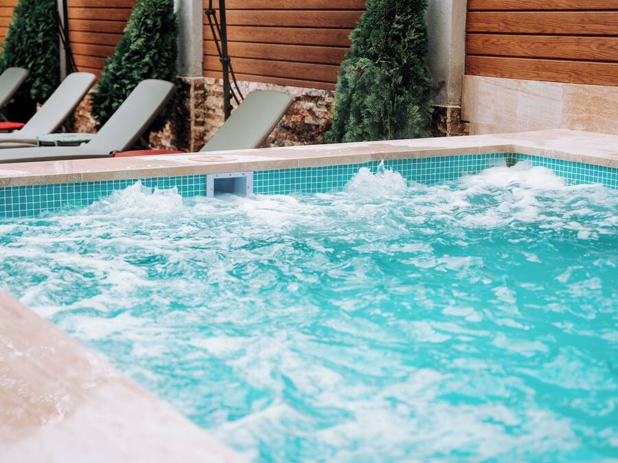 A hot tub with water jets, surrounded by lounge chairs and a wooden wall.
