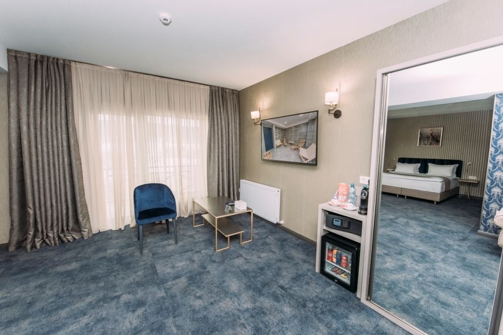 A hotel room with a bed, a desk, a chair, a mirror, and a radiator.