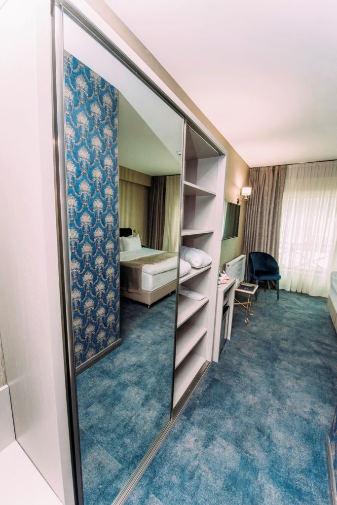 Una habitación de hotel con una cama, un escritorio, una silla, un armario y un espejo.