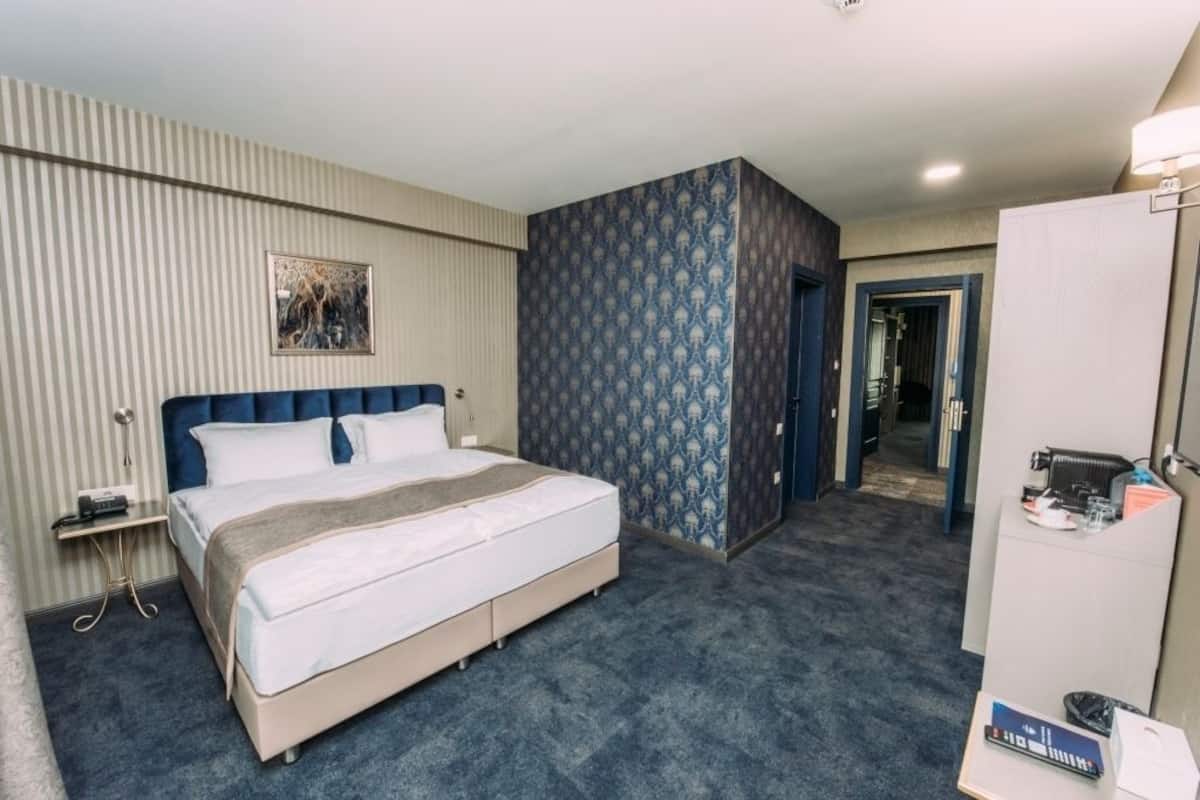 Ein Hotelzimmer mit einem großen Bett, einem Nachttisch, einem Kleiderschrank und einer Tür zu einem weiteren Raum.