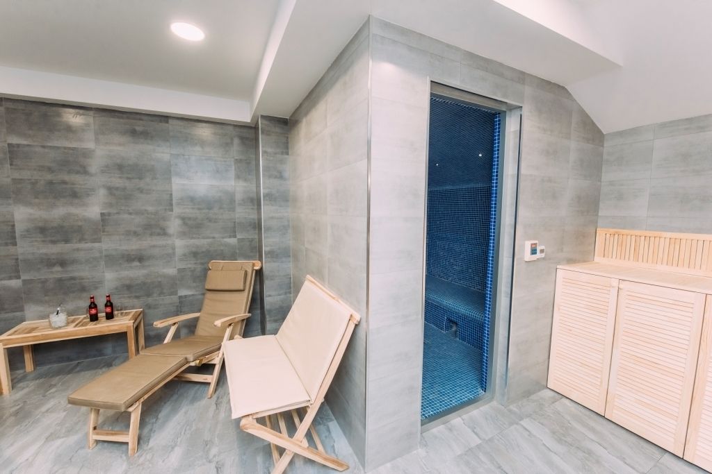 Un spa moderno con dos sillones de madera, una mesita con botellas y una zona de ducha con azulejos azules.