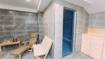 Un spa moderno con dos sillones de madera, una mesita con botellas y una zona de ducha con azulejos azules.