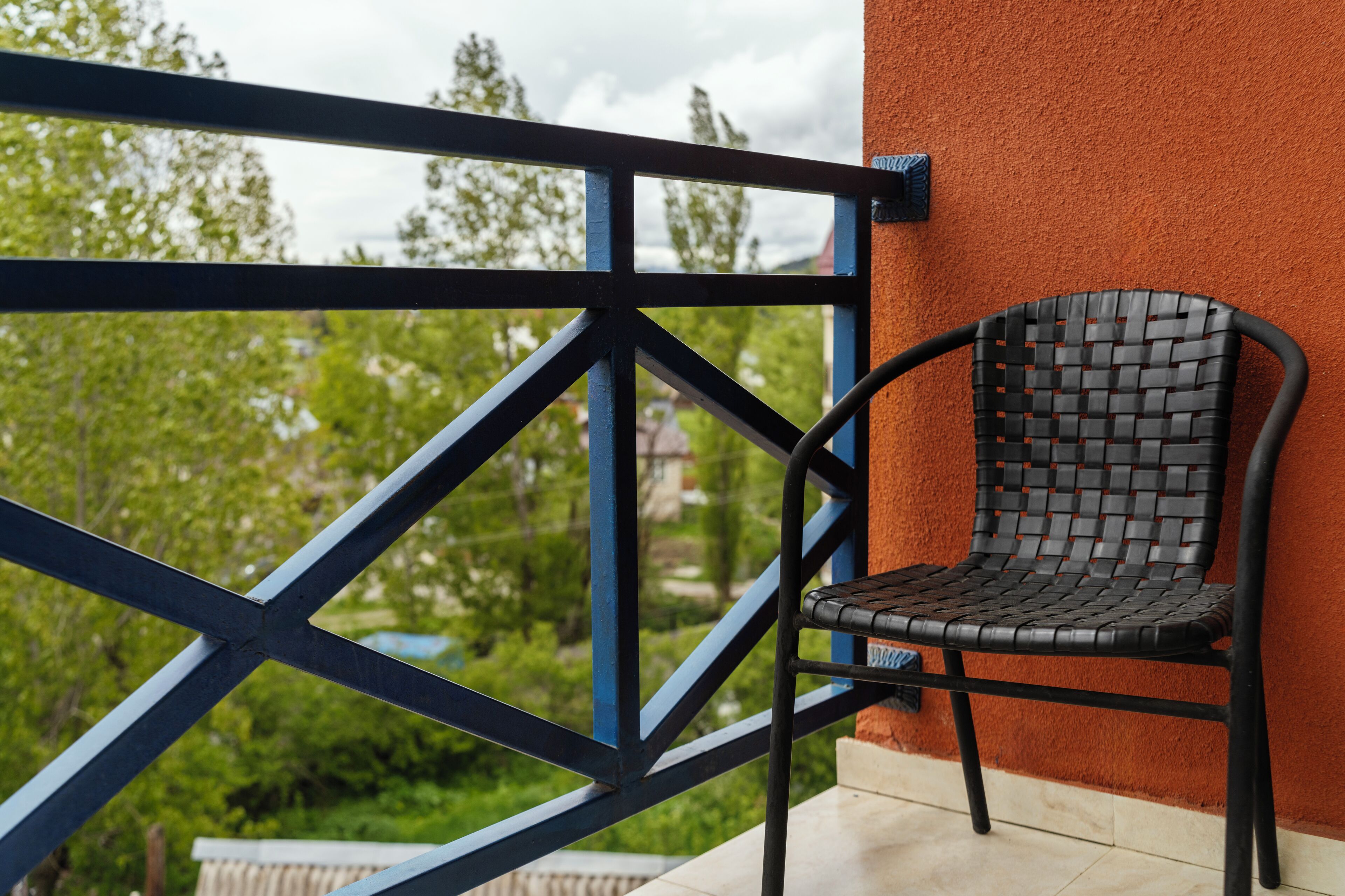 A black woven chair against a red wall, with a blue metal railing in the foreground.